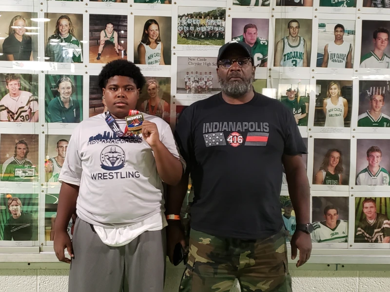 A Young wrestler flaunting his medal with his coach standing beside him