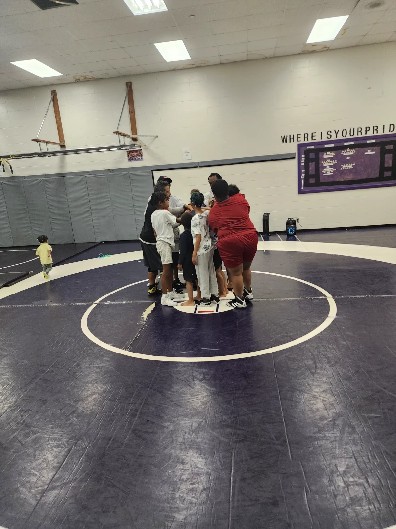 a group of people standing in a circle on a wrestling mat 